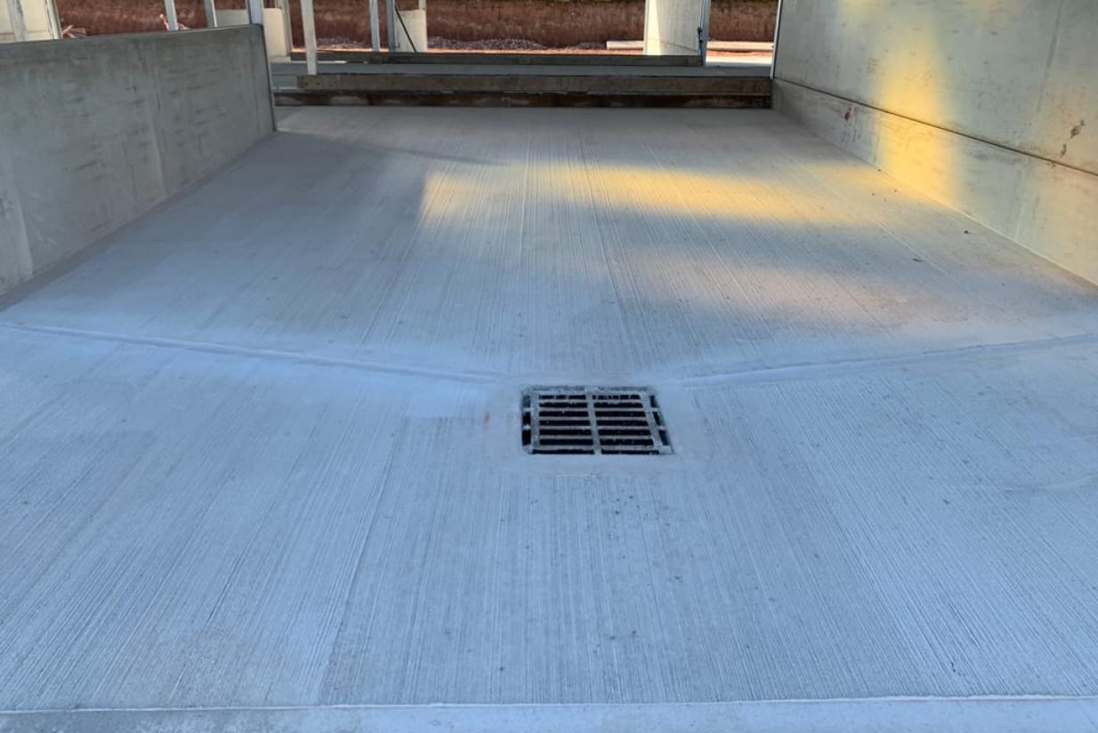 Concrete surface featuring a central drainage grate in an industrial setting.