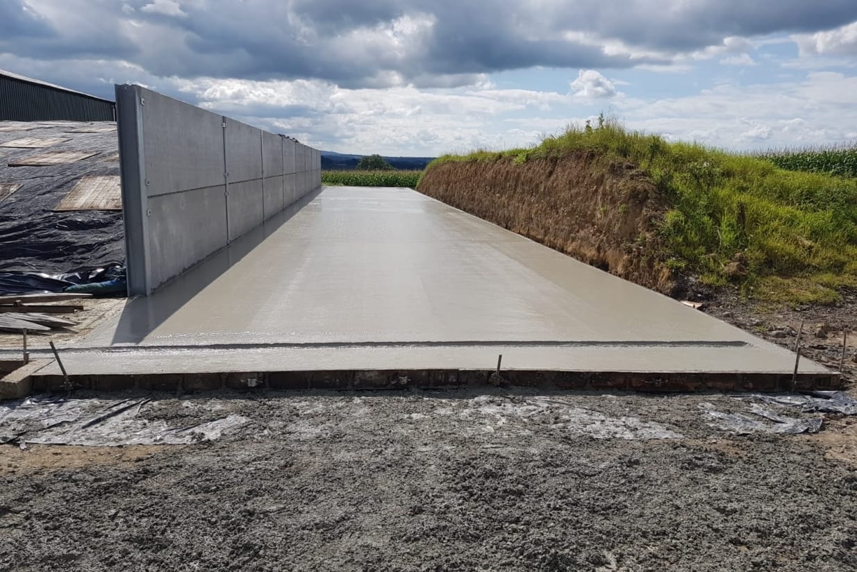 Freshly poured concrete surface adjacent to a vertical retaining wall in a construction area.